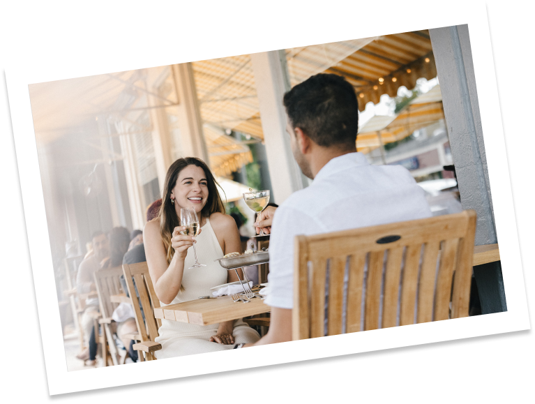 a couple dining outside at a wooden table drinking white wine.
